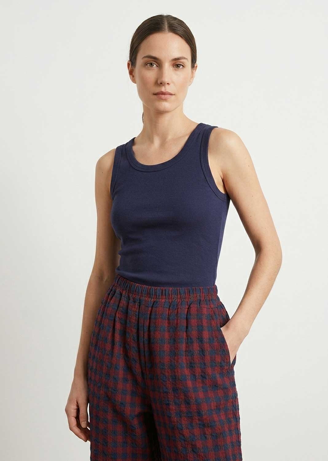 A woman modeling a navy blue ribbed tank top paired with red and navy checkered pajama pants against a plain light gray studio background.