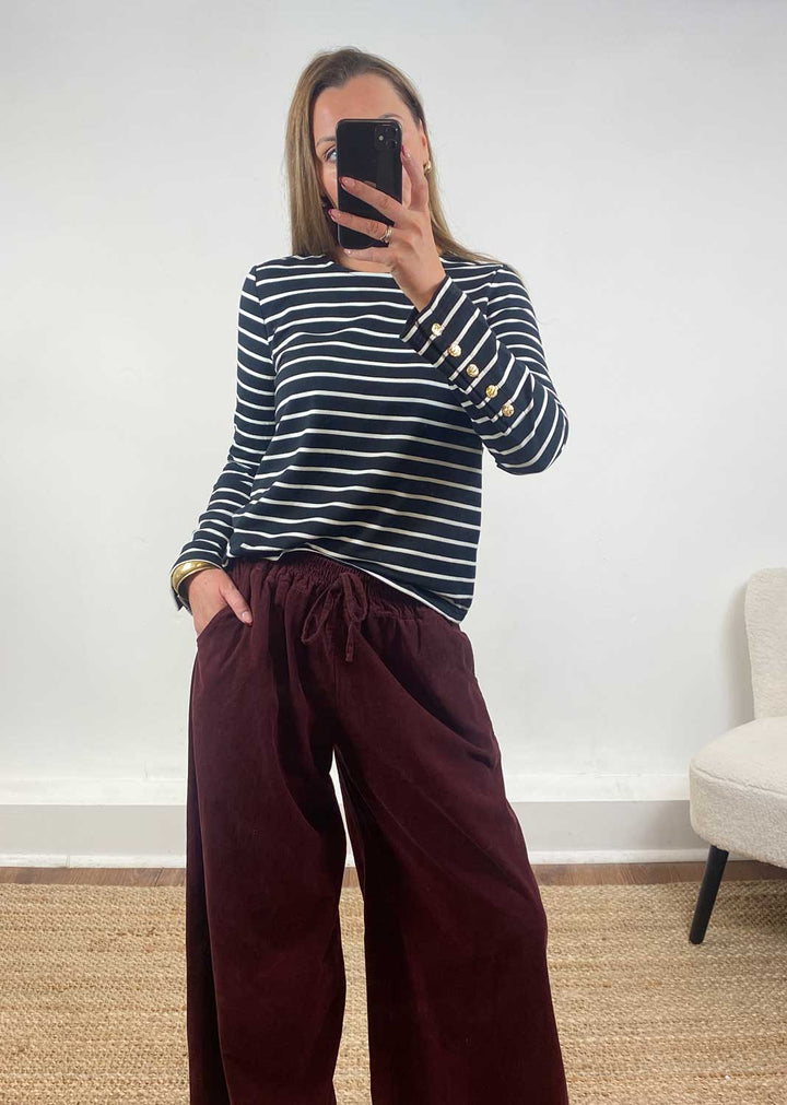 Person wearing a striped sweater and burgundy pants taking a mirror selfie.