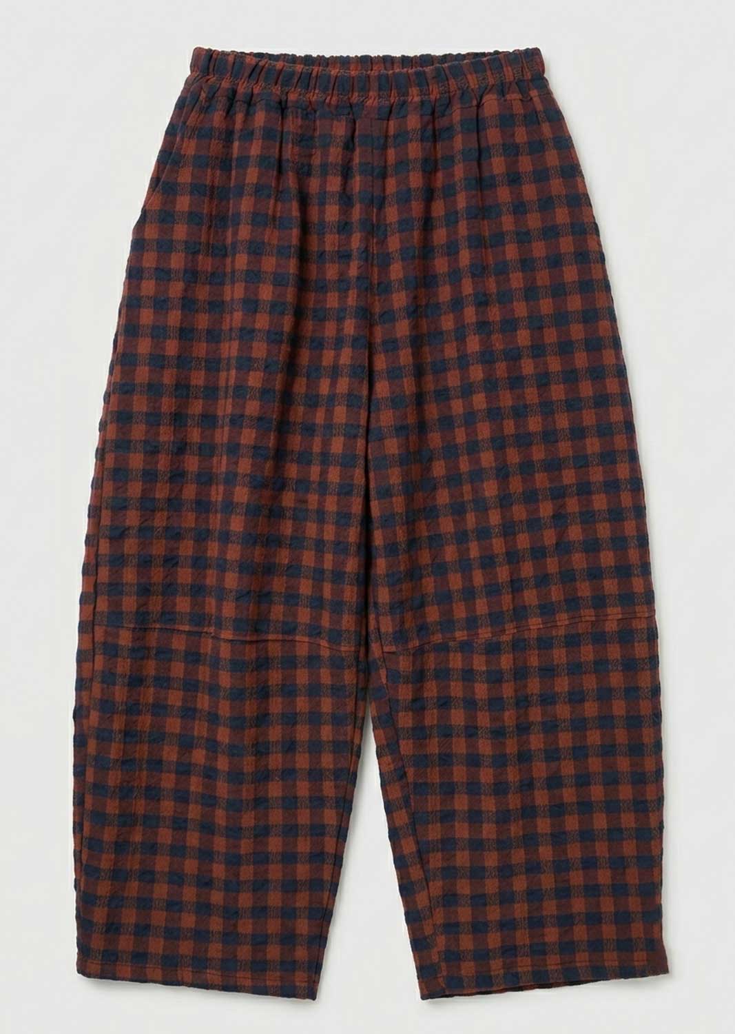 A pair of loose-fitting cropped pants with an elastic waistband, featuring a red and navy blue checkered plaid pattern, shown against a plain light gray background.