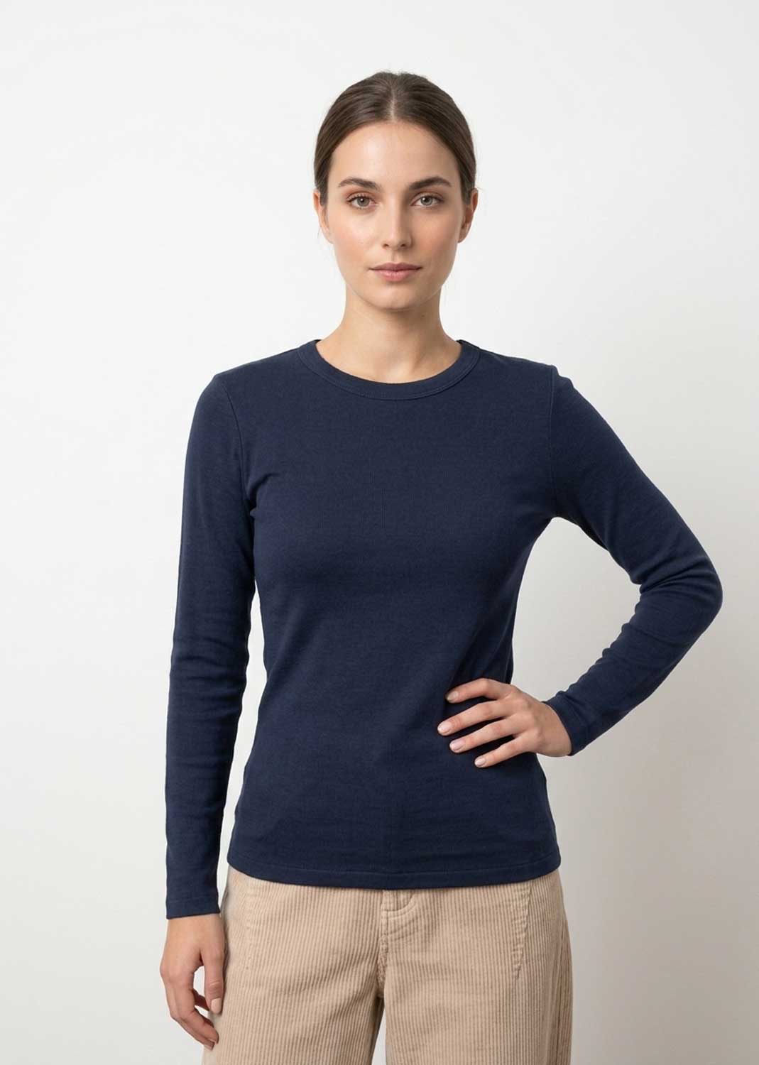 A woman modeling a navy blue long-sleeve crewneck top with beige pants, standing against a light gray studio background.